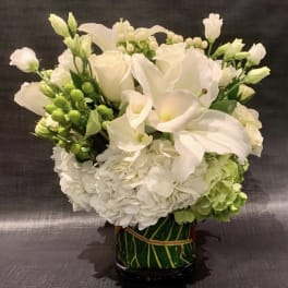 White floral arrangement with calla lilies, roses, and hydrangeas in a green vase