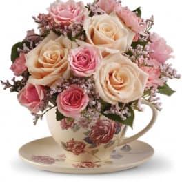 Pink and cream roses arranged in a teacup with matching saucer