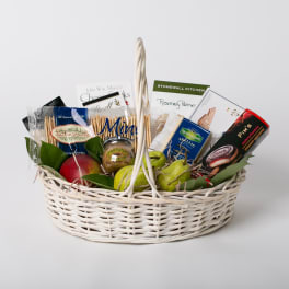 Gift basket with crackers, cheese, fruit, and packaged snacks in a white wicker basket