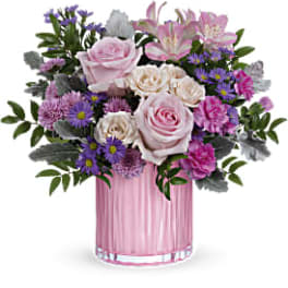 Pink and lavender roses, lilies, carnations, and purple asters in a pink glass cylinder vase