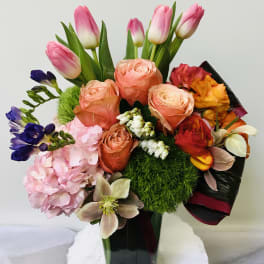 Mixed bouquet of pink tulips, peach roses, and colorful blooms in a glass vase