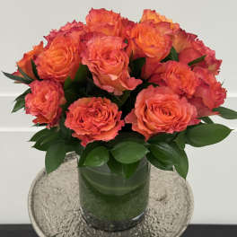 Orange roses arranged in a glass vase with dark green foliage