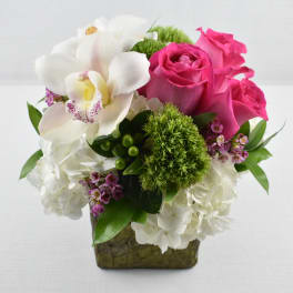 Compact arrangement of white hydrangeas, pink roses, and a white orchid in a green cube vase