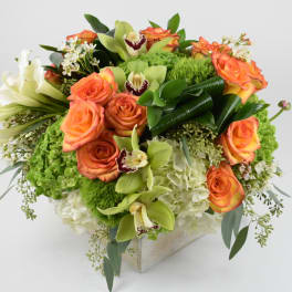 Orange roses and white lilies arranged in a square vase