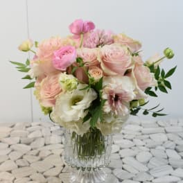 Round arrangement of pale pink and white roses and other blooms in a clear glass vase
