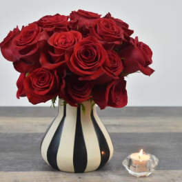 Red rose bouquet in a striped vase beside a lit candle