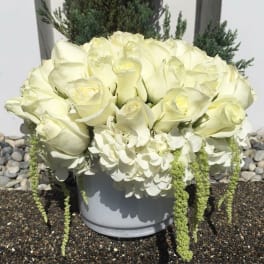White rose arrangement in a gray container with trailing white blooms