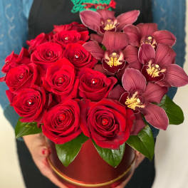 Red roses and burgundy orchids arranged in a round box