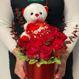 Red roses in a round box with a teddy bear holding a heart