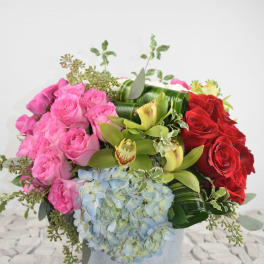 Pink and red roses with blue hydrangea and green orchids in a vase