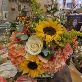 Bouquet with sunflowers, white roses, and peach hydrangeas in a glass vase