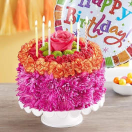 Birthday cake decorated with flowers and candles beside a birthday balloon