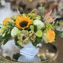 Mixed floral arrangement with a sunflower in a white pedestal vase
