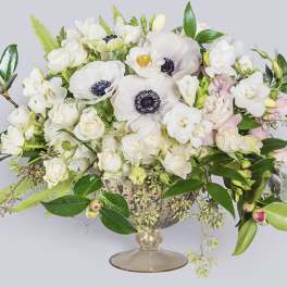 White floral arrangement in a glass compote vase with pink accents