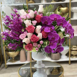 Pink and purple floral arrangement in a white pedestal vase