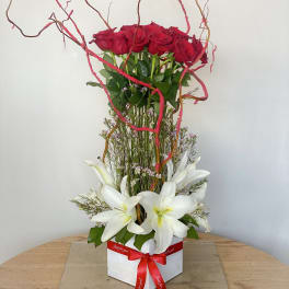 Tall arrangement of red roses and white lilies in a white box with a red ribbon