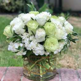 White and pale green roses arranged in a clear glass vase
