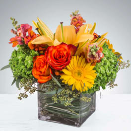 Orange roses and yellow lilies in a square glass vase with green hydrangeas