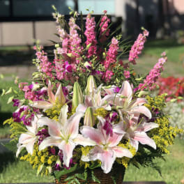 Basket arrangement of pink lilies, purple orchids, and yellow filler flowers
