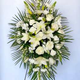 White floral standing spray with lilies and roses on a palm backdrop