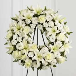White floral wreath with lilies and roses on a black easel