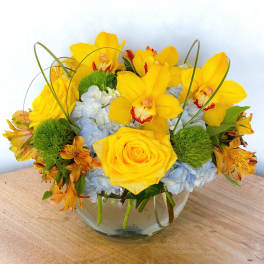Yellow orchids and roses arranged in a glass bowl with blue hydrangeas
