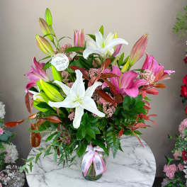 Tall bouquet of pink and white lilies in a glass vase with ribbon