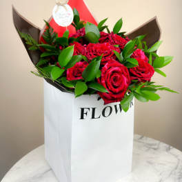 Red roses arranged in a white gift bag with green foliage