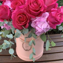Hot pink roses and pale pink hydrangea in a blush hatbox with trailing eucalyptus.