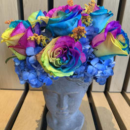 Rainbow-colored roses and blue hydrangeas in a gray bust vase