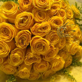 Large bouquet of yellow roses with a small gold crown accent on yellow wrapping