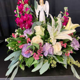 Large floral arrangement with white lilies, roses, and pink blooms around an angel figurine