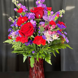Red roses and purple mixed flowers in a red glass vase