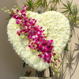Heart-shaped white floral arrangement with a magenta orchid spray