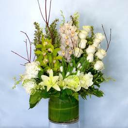 White roses, orchids, and lilies arranged in a green glass vase
