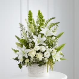White lilies and roses in a white basket with green accents