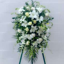 White floral standing spray with lilies and roses on a green easel