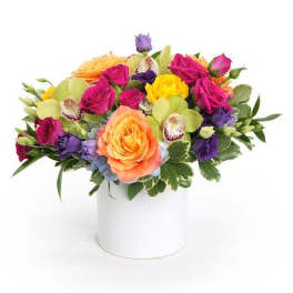 Low mixed arrangement of bright roses, orchids, and lisianthus in a white cylinder vase