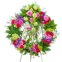 Bright standing wreath of pink roses, green and red blooms on a metal easel.