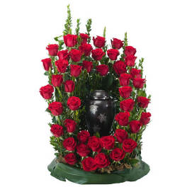 Tall cremation arrangement of red roses surrounding a dark urn on a green base