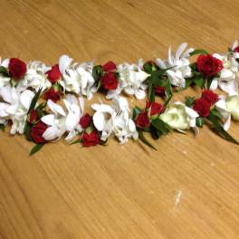 Red and white floral lei with ribbon on a wooden surface