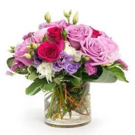 Round arrangement of pink and purple roses with white and lavender blooms in a clear glass vase