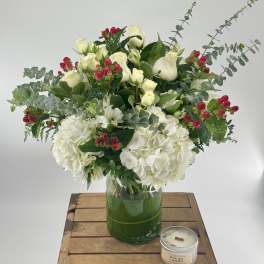 White floral arrangement in a glass vase with red berry accents