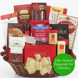 Wicker gift basket filled with assorted chocolates, snacks, cheese, and a bow.