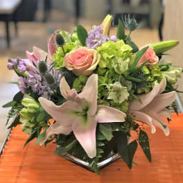 Low arrangement of pink lilies, roses, and green hydrangeas in a clear glass vase