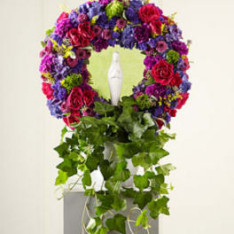 Vibrant circular wreath of purple and red flowers around a white statue with cascading ivy