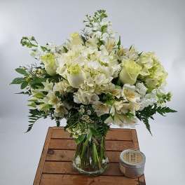 White floral arrangement in a clear glass vase with a small candle beside it.