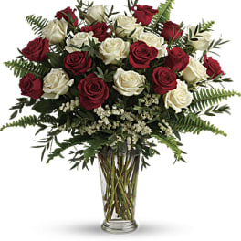Tall arrangement of red and white roses with ferns in a clear glass vase