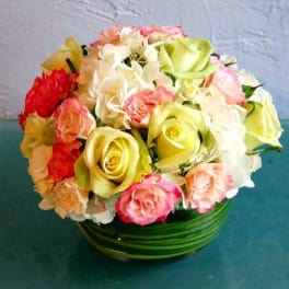 Round arrangement of white and green roses with pink accents in a low glass bowl with green bands.