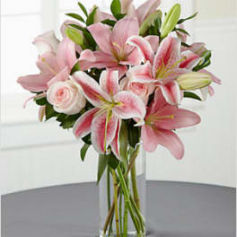 Tall clear vase of pink lilies and roses on a gray tabletop